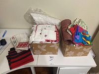 Boxes containing folded tablecloths, placemats, aprons, and napkins with traditional embroidered patterns and colorful fabric pieces.