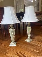 Pair of matching 32 inch tall lamps with heavy green stone bases and white fabric shades. Lamps are placed on hardwood floor near wooden furniture.