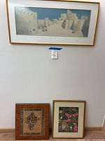 Overview showing one large framed print depicting adobe houses and two other smaller framed artworks leaning against the wall