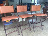 Front and side view of three matching metal and leather bar stools arranged in a row on a floor with visible carpet texture.