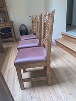 Side view of three hardwood chairs showing maroon leather cushions and carved wooden backs with southwest motifs.
