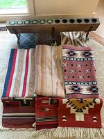 Long wooden votive candle holder on stand with multiple small candles and southwestern rugs arranged beneath it.