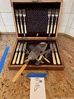 Full set of antique dessert forks, knives, pie server and spoon inside original wooden box with satin lining.