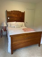 Full view of antique carved oak double bed made with white linens and pink blanket folded on top.