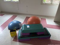 Set of two adjustable step platforms with purple stacking blocks, a blue Bosu ball, and a yellow box containing resistance bands.