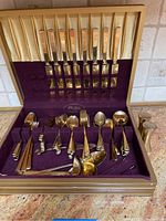 Full view of the open flatware box showing the complete gold toned flatware set including knives, forks, spoons, serving pieces and salt and pepper shakers.