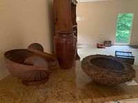 Photo showing all three items side-by-side on a granite countertop: the ceramic vase in the center, with the wooden slatted basket on the left and the twig bundle basket on the right.