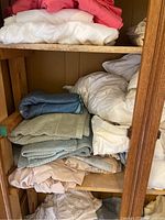 Shelves filled with folded linens including sheets, comforters, and towels in various colors like white, coral, blue, beige, and cream.