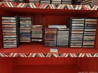 Shelving unit with stacks of over 100 CDs in jewel cases, spanning three shelves with visible artist and album titles.