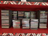 A shelf with multiple stacks of CDs in jewel cases, organized vertically and horizontally with over 150 CDs visible.