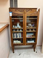 Full front view of oak china cabinet with contents inside, showing glass front doors and carved ornamentation.