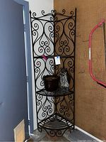 Full view of black wrought iron corner shelf with decorative scrollwork, three tiers, and items displayed on shelves.
