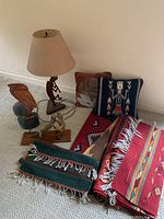Photo shows 2 pillows, multiple Southwestern textile rugs in red, orange, and green tones, rustic metal lamp with fabric shade, and wooden pelican sculpture.
