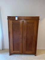 Front view of tall oak storage cabinet showing double paneled doors and carved top molding.
