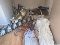 Multiple cat door draft stoppers lined up along with leopard statues, a large stuffed insect toy, and a white sheer robe lying on floor