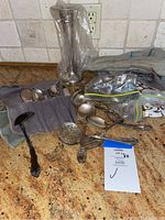 Various antique silver serving utensils and kitchen pieces displayed on a counter including ladles, spoons, and a silver container.
