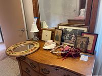 Overall view of dresser top showing mirror, crystal lamp, several framed vintage prints, and floral headpieces.