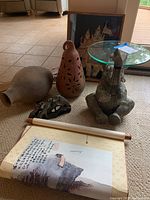 Group shot showing ceramic elephant table with glass top, shadow box art, terracotta pear sculpture, laying urn, metal cheetah sculpture, and Asian scroll on carpet.
