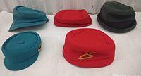Five vintage hats in various colors and styles arranged on white surface.