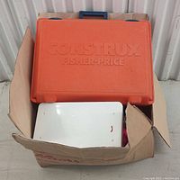 Closed orange plastic case labeled 'CONSTRUX FISHER-PRICE' inside a cardboard box