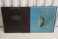 Two vinyl album covers side by side: Eagles "The Long Run" on black cover and "Greatest Hits" with blue cover and eagle sculpture logo.