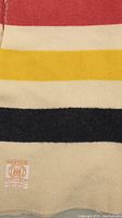 Close-up photo of the blanket stripes showcasing red, yellow, and dark blue wool stripes with texture details and part of sewn label.