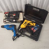 Photo showing the three tools together: Mastercraft blue drill, yellow hand drill in black case, and Skil jigsaw on top of its box.