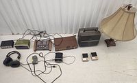 Photo showing all items in the lot: audio equipment including a Realistic stereo pre-amplifier, headphones, cassette player, portable speaker, two handheld devices, and a beige table lamp.