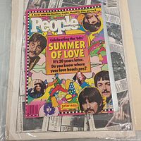 Colorful People Weekly magazine celebrating 1960s Summer of Love with Beatles and other iconic figures on cover, resting on a backdrop of open newspaper pages.