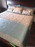 Overview of king size bed with damask comforter, light blue blanket, and five decorative pillows