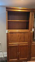Tall wooden cabinet with open upper shelves and closed lower doors with brass knobs