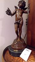 Full view of bronze cherub statue showing front and side, mounted on a round base.