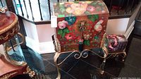 Full view of both chests, large on stand and small beside it, showing floral painted curved tops and metal tassel lock.