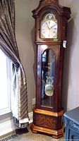 Front view of the wooden grandfather clock showing hood, dial, pendulum case and base