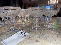 Group photo of nine crystal champagne saucers with one chipped base visible. Displayed on a granite countertop with green tape markings in the background.