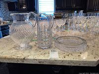 Photo showing two clear glass jugs with distinct patterns and a clear textured glass bowl on granite counter.