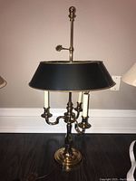Full view of brass table lamp with black shade and three white candle-shaped lights on brass arms.