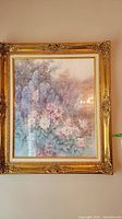 Framed floral print in ornate gold frame hung on wall, showing full view of artwork and frame.