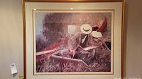 Front view of large framed print showing couple by canoe in grass, with gold ornamental frame and double matting