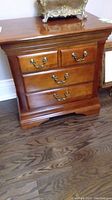 Full front view of the wood side table showing three drawers and ornate metal handles.