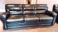 Front view of black three-seater leather sofa on a light carpeted floor.
