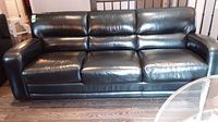 Full view of black leather three-seater sofa with padded armrests, cushioned backrest, and seat cushions.