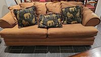 Front view of the brown two-seater sofa with cushions showing fabric and decorative trim.