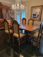 Dining table with 6 matching chairs arranged in a room with chandelier overhead.