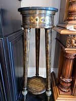 Front view of the stone top side table showing the four legs, lower shelf, and ornate decorative painted designs and metal studs around the top apron under the stone top.