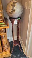Full view of the tall wooden plant stand with a round top displaying a decorative item on top, showing the legs and small circular bottom shelf