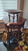 Full view of wooden hexagonal table with dark finish, ornate carvings, and turned legs, shown with decorative brass bowl on top and other decorative items around the base.