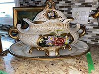 View of the tureen on the matching tray with serving spoon inside, showing crackled glaze, floral painting, and gold accents.