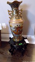 Full view of the large decorative Asian vase on top of the black round wooden stool, showing vase design and stool details.