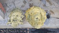 Two stone face sculptures resting on stone floor showing details of facial features and texture.